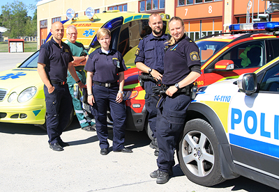 Gruppbild med bilar och personal från ambulans, räddningstjänst och polis.  Tre herrar och två damer, samt tre bilar.