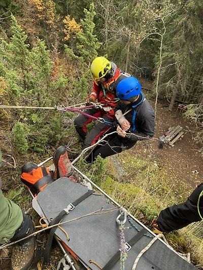 2 bergsklättrare med rep och bår som hjälper person