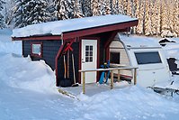Ett spiketält i anslutning till en vid husvagn i ett snöigt landskap.