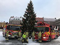 Styrkan på 6 man står framför sina två röda brandbilar framför den stora julgranen på Stortorget i Östersund.